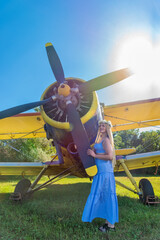 A cute woman is standing next to an plane. A woman with a wreath of flowers on her head