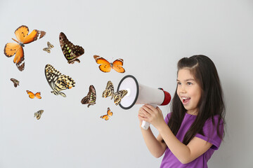 Screaming little girl with megaphone and flying butterflies on light background