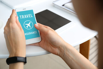 Woman with mobile phone applying for travel insurance online at home