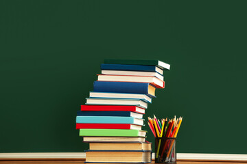 Stack of books and holder with pencils on color background