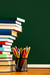 Stack of books and holder with pencils on color background