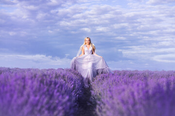 Fototapeta premium beautiful woman in a lush long dress runs in a lavender field. A girl in the image of a fairy and a princess of flowers.