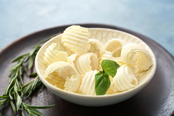 Bowl with fresh butter, basil and rosemary on color background