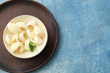 Bowl with fresh butter and basil on color background