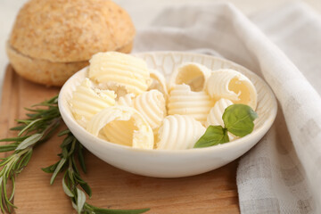 Bowl with fresh butter, bread, basil and rosemary on wooden board