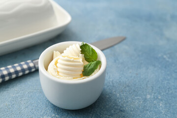 Bowl with fresh butter and basil on color background