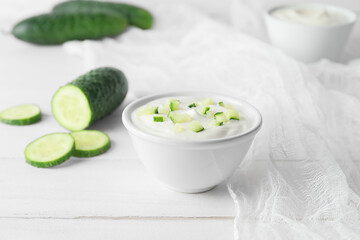 Bowl of tasty sour cream and cucumber on white wooden background