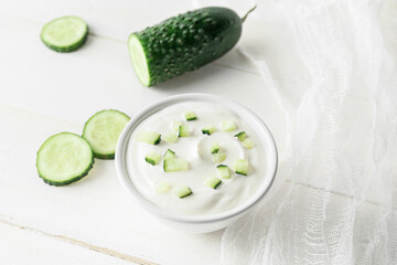 Bowl of tasty sour cream and cucumber on white wooden background