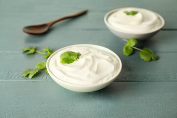 Obraz na płótnie Canvas Bowls of tasty sour cream and herbs on color wooden background