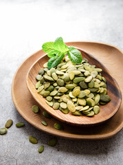 Wooden plate with pumpkin seeds on a gray concrete background