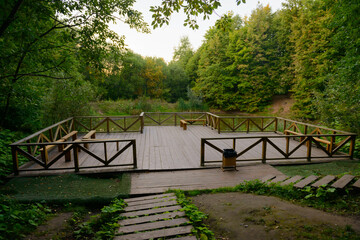 A small observation deck made of wood in the middle of the forest with a pond on a summer evening