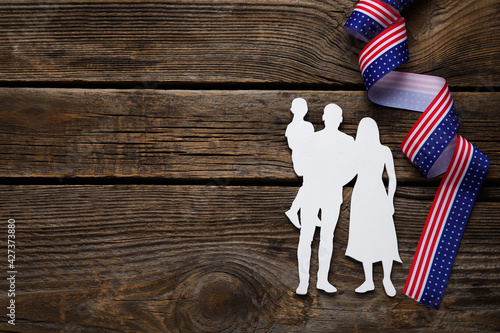 Ribbon in colors of USA flag and figure of family on wooden background
