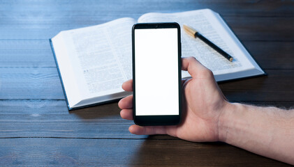 A man businessman is holding a mobile phone, on a wooden table. White blank screen. Empty table. Office workplace