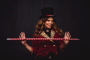 Female magician illusionist circus with wand in theatrical clothes shows and smiles, on black...
