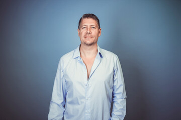Middle aged business man with blue shirt posing against blue background in the studio