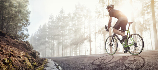 Cyclist with a racing bike riding on a foggy forest road