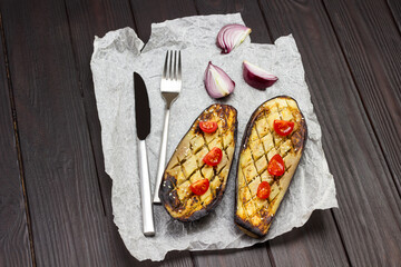 Baked eggplant with onions and tomatoes, knife and fork on paper