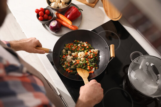 Man stirring mix of fresh vegetables in frying pan, above view