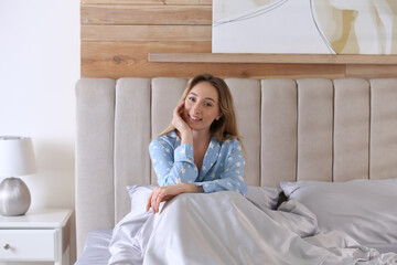 Young woman sitting on comfortable bed with silky linens