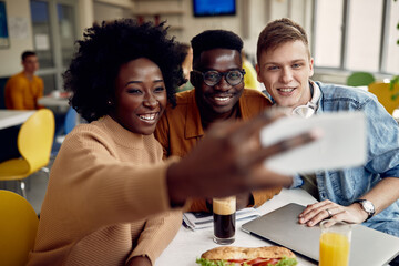 Group of happy university friends taking selfie on a break in cafeteria.