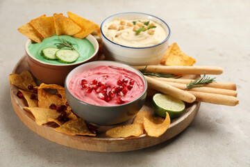 Different kinds of tasty hummus served with snacks on light table
