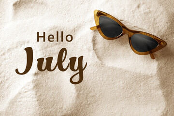 Hello July. Stylish sunglasses on sand, top view
