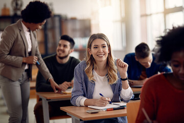 Happy female student writing notes while during lecture in the classroom.