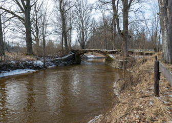 a continuous boulder stone bridge with a brick used for masonry, early spring, bare trees, snow plan on the ground, Stone arch bridge over the river Kuja, Madona, Latvia © ANDA