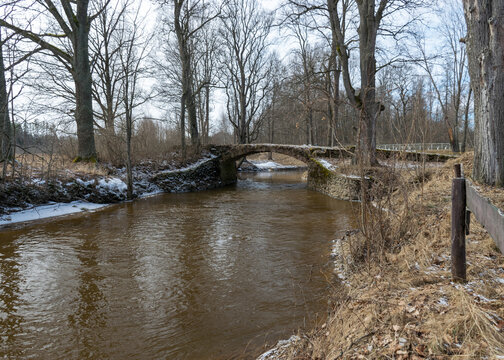 a continuous boulder stone bridge with a brick used for masonry, early spring, bare trees, snow plan on the ground, Stone arch bridge over the river Kuja, Madona, Latvia
