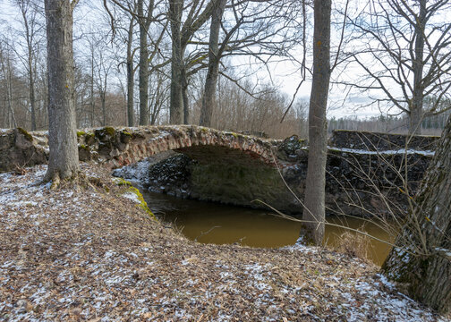 a continuous boulder stone bridge with a brick used for masonry, early spring, bare trees, snow plan on the ground, Stone arch bridge over the river Kuja, Madona, Latvia