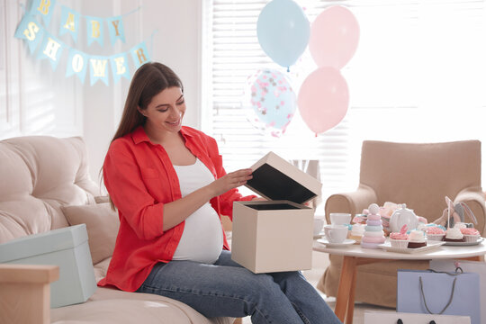 Happy pregnant woman with gift box in room decorated for baby shower party