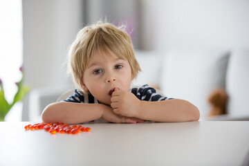 Cute little child, toddler boy, eating alfa omega 3 child suplement vitamin pills at home