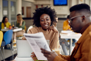 African American female student and her friend learning on break in cafeteria.