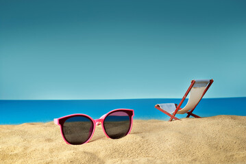 Pink glasses on the sand close up. Glasses on a beach chair background. Beach chairs on a background of blue water and sky. Summer, sea and vacation concept.
