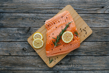 Raw salmon fillet with lemon, rosemary and pepper on cutting board. Fresh organic wild Atlantic fish on wooden background. Top view. Mediterranean cuisine. Healthy and diet food concept.