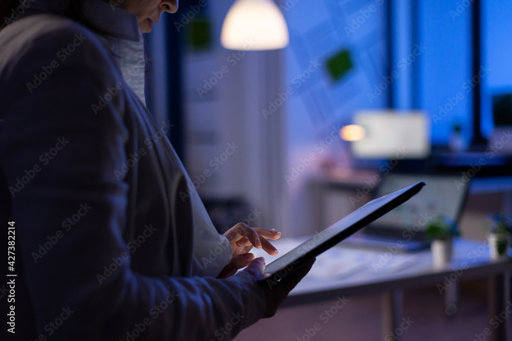 Aufkleber Close-up of woman hands typing on tablet checking financial graphs standing in start-up office late at night. Manager using social network, texting and blogging working overtime for job