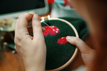 Woman's hands sewing on green cloth. Embroidery process with cotton thread of mushrooms hat. Needlework concept. Craft and handmade.