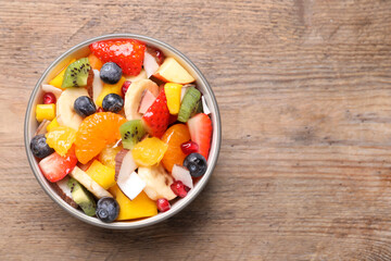 Delicious fresh fruit salad in bowl on wooden table, top view. Space for text