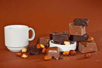 Chocolate on a pile close up. Different types of chocolate on a brown background. Nuts and a white mug near the chocolate.