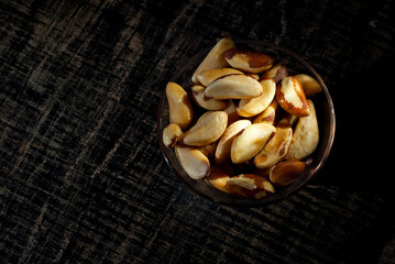 Brazil nuts in a glass bowl on a wooden table. Nuts on a black shabby board. Contrasting dramatic light as an artistic effect.