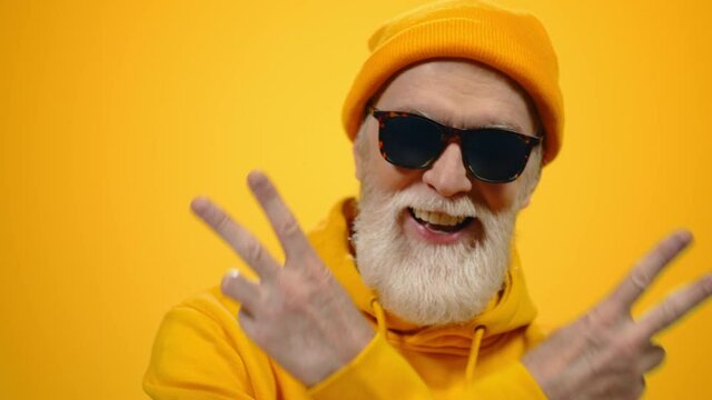 Cheerful Old Man Raising Hands Indoors. Joyful Guy Posing To Camera In Studio.