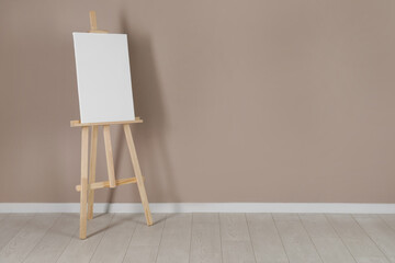 Wooden easel with blank canvas near beige wall. Space for text