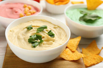 Different kinds of tasty hummus with nachos on white wooden table, closeup