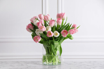 Beautiful bouquet of tulips in glass vase on white marble table