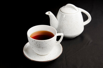 White tea cup with tea pot over black background.