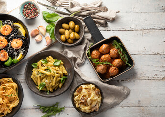 Assortment of Italian pasta with traditional snacks and sauces for dinner on white wooden background.
