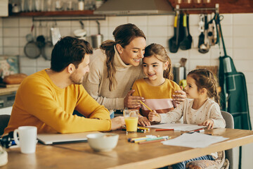 Happy parents enjoying with their small daughters who are coloring on the paper at home.