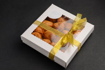 Cardboard box filled with cookies over black background. Pastry delivery box, takeaway concept.