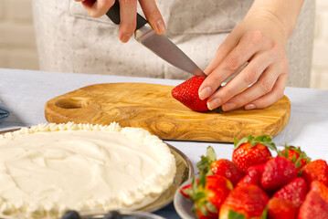 woman baker cuts strawberries for strawberry cake. Homemade strawberries cake made from meringue cake and cream with strawberries. home cooking concept