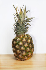 A whole pineapple lies on a wooden surface on a white background, close-up, side view. Ripe, fresh fruit. Pineapple with peel and long bushy tail. Vitamins. Benefit. Healthy eating. Exotic fruit.